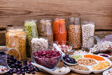 Various legumes: beans, chickpeas, lentils in glass jars on wooden background. Healthy vegetarian food