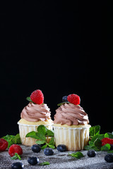 Two handmade cupcakes with raspberries on a black background. Still life concept
