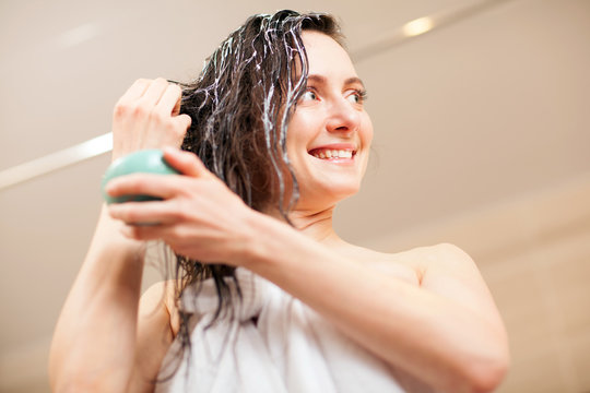 Smiling young woman applying hair mask in a bathroom