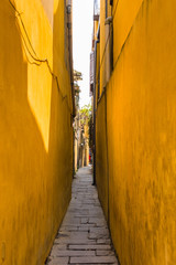 tiny alley lined with bright golden yellow buildings connecting two streets in old Hoi An, Vietnam