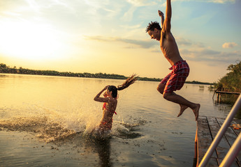 Group of friends jumping into the lake from wooden pier.Having fun on summer day.