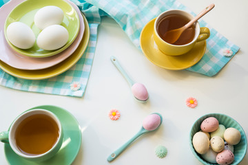 flat lay Easter breakfast with colored eggs in bowl, blue napkin, cup of tea on white table