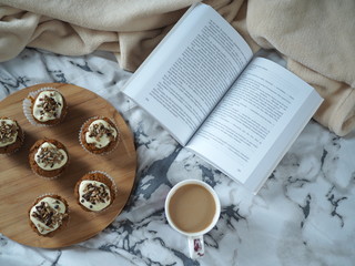 Książka w przytulnym łóżku, kawa i babeczki