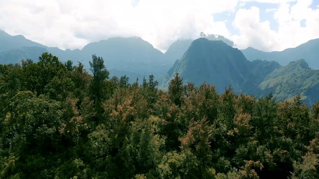 Drone flight low over trees reveals the dramatic mountain landscape surrounding the town of Hell-Bourg on Reunion Island