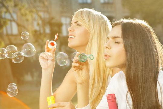 Bubbles. Horizontal shot of mother and daughter blowing soap bubbles together sitting in the park