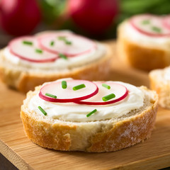 Bread slices with cream cheese, radish slices and chives on wooden board, photographed with natural...