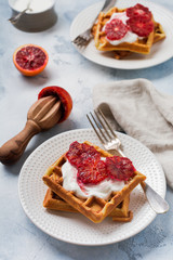 Waffles with yogurt sauces and red Sicilian orange sauces on light old background. Top view.