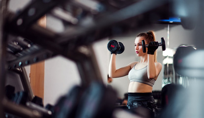Fototapeta na wymiar Young girl or woman with dumbbells, doing workout in a gym.