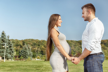 Fototapeta na wymiar Together forever. Handsome man and his beautiful pregnant wife holding hands and looking each other in the eyes