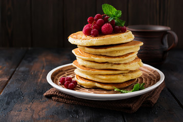 Stack of homemade little pancakes with honey, fresh raspberries and red currants on an old wooden background. Selective focus.