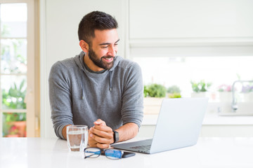 Handsome hispanic man working using computer laptop looking away to side with smile on face,...