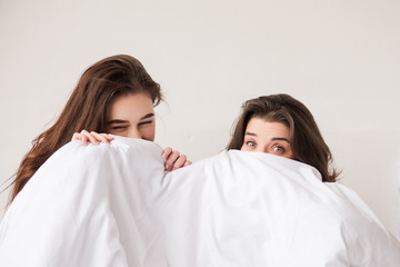 Two sweet girls hiding under white blanket