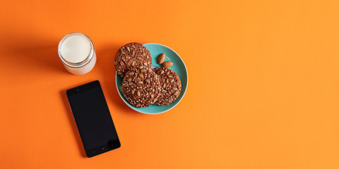 Oatmeal cookies with nuts on a plate, cup of milk, phone 