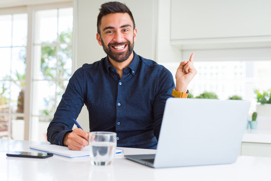 Handsome hispanic man working using computer and writing on a paper very happy pointing with hand and finger to the side
