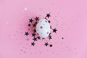 Egg decorated with dots on pink background with star confetti, Easter concept.