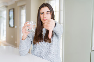 Beautiful young woman drinking a fresh glass of water with angry face, negative sign showing dislike with thumbs down, rejection concept