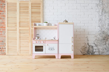Play furniture for children. Pink and white wooden toy kitchen with sink, oven and fridge in light room