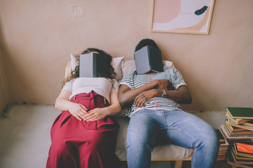 Funny interracial couple sitting in chair in studio and sleeping with books on their faces. Tired...