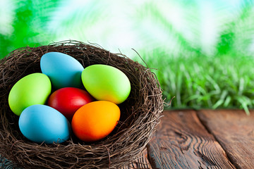 Colored Easter eggs in the nest on wooden table and nature background