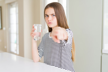 Beautiful young girl kid drinking a fresh glass of water pointing with finger to the camera and to you, hand sign, positive and confident gesture from the front