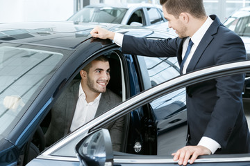 This is the one. Horizontal portrait of a handsome young businessman sitting in the car and talking to a car dealer standing near