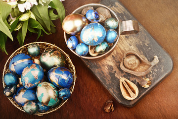 Obraz na płótnie Canvas Painted colored Easter eggs in golden bowl and copper mug near bouquet of flowers on red animal skin. Boho stile.