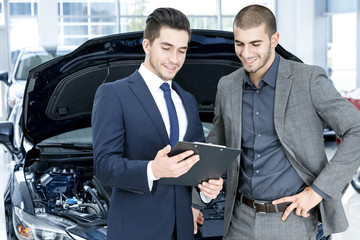 This is what he needs. Smiling car salon manager talking to a happy client in a suit