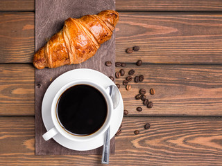 Coffee cup, beans and croissant on wooden background on the table. Perfect breakfast in the morning. Rustic style, top view