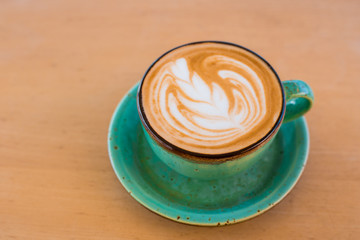 One cup of cappuccino with latte art on wooden background, greenery ceramic cup, place for text