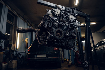 Car engine with hinged equipment suspended on a hydraulic hoist in the workshop