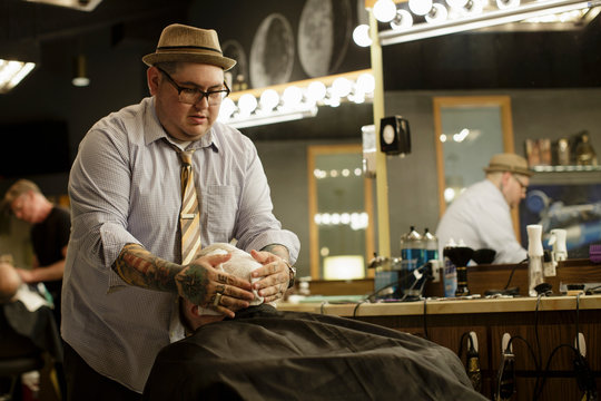 Tattooed barber places hot towel on client's face
