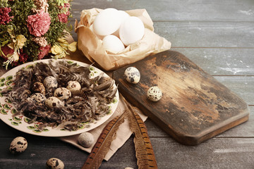 Open eco-friendly ceramic plate with feathers and quail eggs on rough dyed wooden background. Eggs...