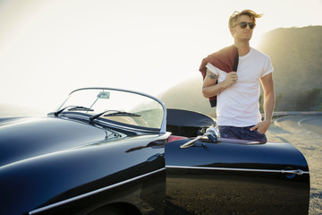 Stylish young man in white t shirt stands next to convertible