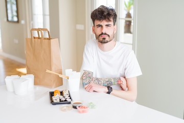Young man eating asian sushi from home delivery skeptic and nervous, disapproving expression on face with crossed arms. Negative person.