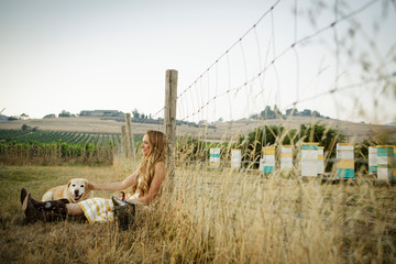 Woman and dog sit by woven wire fence