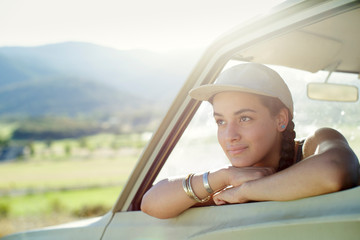 Young woman wears baseball cap and leans out car window