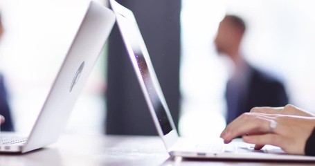 4K Business executives typing on laptops with colleagues blurred in background
