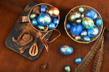 Painted colored Easter eggs in golden bowl and copper mug on red animal skin. Boho stile.