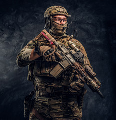 The elite unit, special forces soldier in camouflage uniform holding an assault rifle with a laser sight. Studio photo against a dark wall