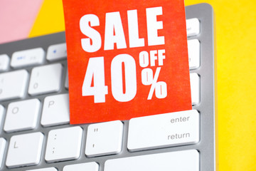 Red paper label with an inscription "sale off 40%" on a white keyboard on a yellow background.