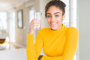 Young african american woman drinking a glass of fresh water with a happy face standing and smiling with a confident smile showing teeth