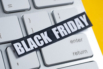 Black Friday sticker on a white keyboard. Yellow background.