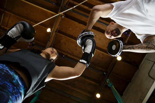 View of woman boxer hitting woman boxer pads from below