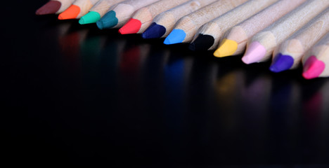Colored pencils on a black background close-up in macro photography.