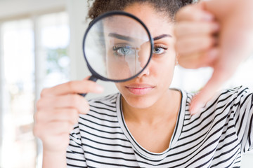 Young african american woman looking through magnifying glass with angry face, negative sign...