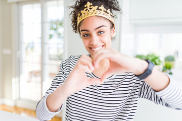 Fototapeta na wymiar Young african american girl wearing golden queen crown on head smiling in love showing heart symbol and shape with hands. Romantic concept.