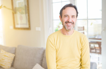 Handsome middle age man sitting on the sofa relaxed and smiling at the camera at home smiling at the camera at home