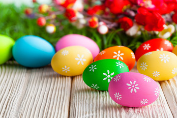 Fototapeta na wymiar Colorful painted Easter eggs and flowers on wooden table and grass background
