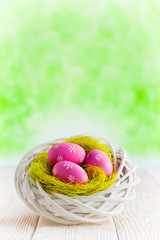 Three pink Easter eggs in the nest and wooden table on green abstract background