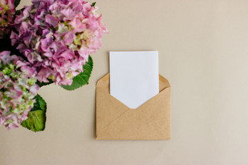 On a light background, an empty white card with an envelope of Kraft paper. Pink, purple, purple hydrangea flowers.